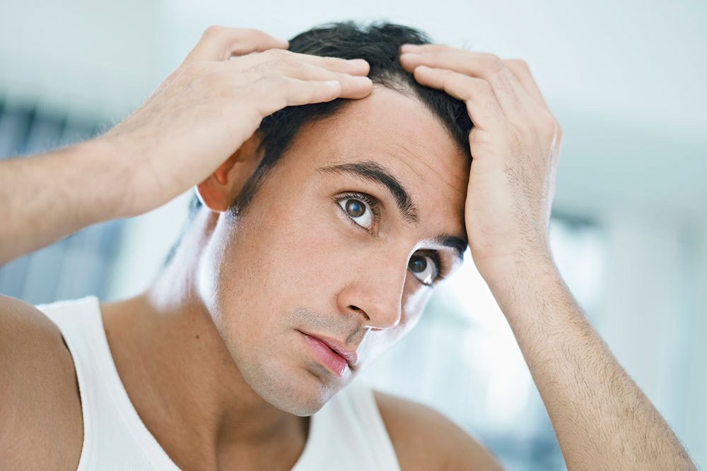 man inspecting possibly receding hairline in mirror