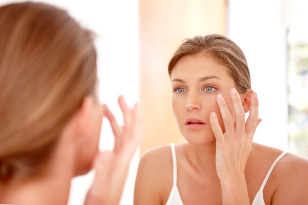 Woman looks at skin in mirror after radiofrequency microneedling treatment