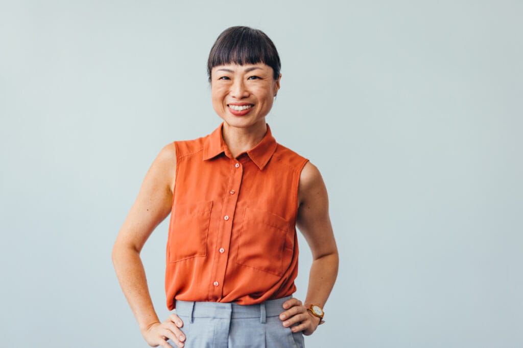 Asian woman in her 40s smiling with hands on hips